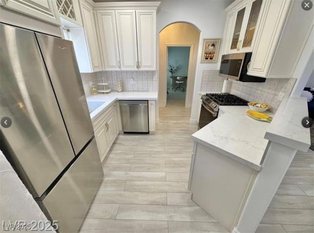 9000 Las Vegas Blvd Unit 2060, Las Vegas, NV 89123 - kitchen featuring appliances with stainless steel finishes, arched walkways, a peninsula, glass insert cabinets, and tasteful backsplash