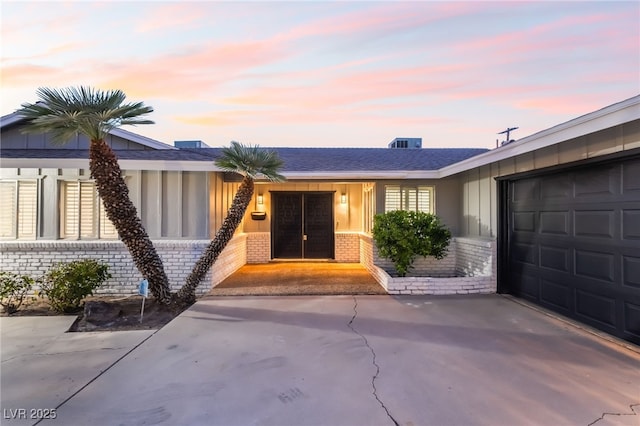 1009 Ironwood Dr, Las Vegas, NV 89108 - exterior entry at dusk with brick siding, an attached garage, driveway, board and batten siding, and a shingled roof