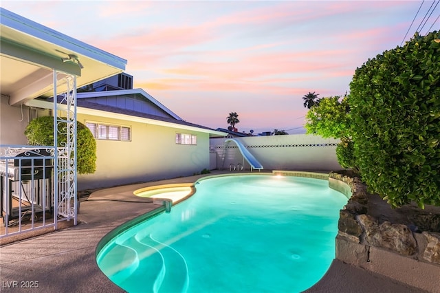1009 Ironwood Dr, Las Vegas, NV 89108 - pool at dusk with a water slide, a fenced backyard, and a pool with connected hot tub