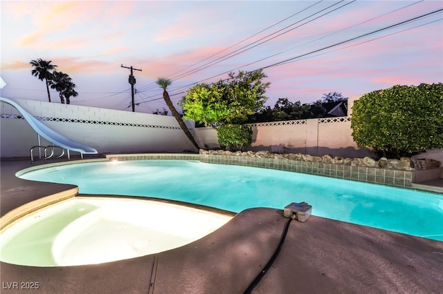 1009 Ironwood Dr, Las Vegas, NV 89108 - pool at dusk featuring a water slide, a fenced backyard, and an in-ground hot tub