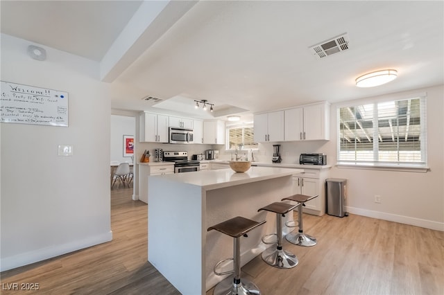 5676 Birchwood Cir, Las Vegas, NV 89120 - kitchen featuring appliances with stainless steel finishes, white cabinetry, a kitchen breakfast bar, light countertops, and light wood-type flooring