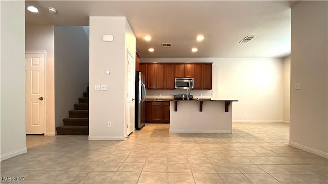 7469 Paces Mill Ct, Las Vegas, NV 89113 - kitchen with stainless steel appliances, dark countertops, a kitchen bar, an island with sink, and light tile patterned floors