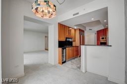 2877 Paradise Rd Unit 904, Las Vegas, NV 89109 - kitchen featuring light colored carpet, a tray ceiling, dark countertops, a chandelier, and brown cabinetry