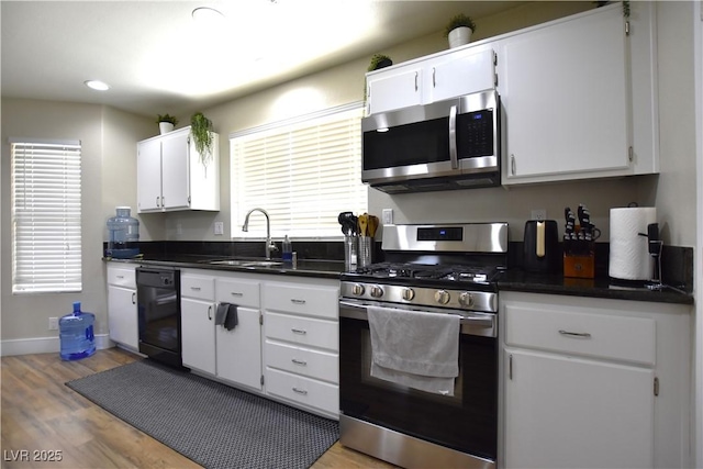 6628 Ives Ave, Las Vegas, NV 89108 - kitchen featuring appliances with stainless steel finishes, light wood finished floors, white cabinetry, and dark countertops