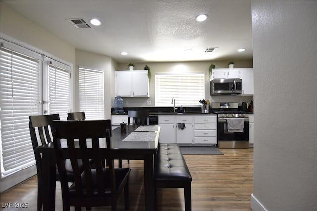 6628 Ives Ave, Las Vegas, NV 89108 - kitchen featuring stainless steel appliances, dark countertops, wood finished floors, white cabinetry, and recessed lighting