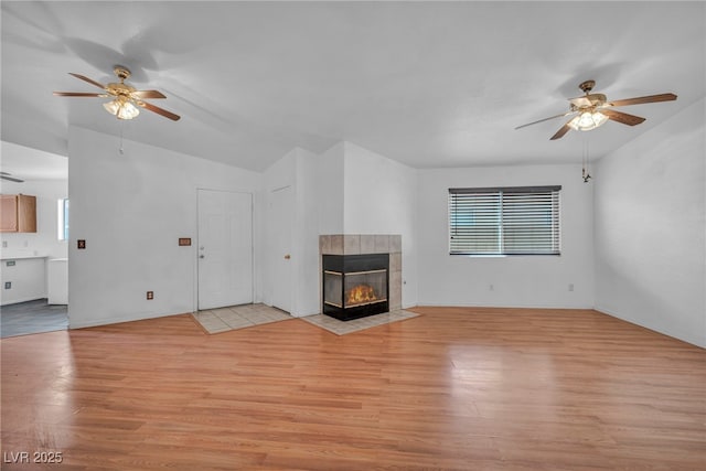 2165 Saint Paul Way, Las Vegas, NV 89104 - unfurnished living room with a ceiling fan, light wood-style flooring, a tiled fireplace, and vaulted ceiling