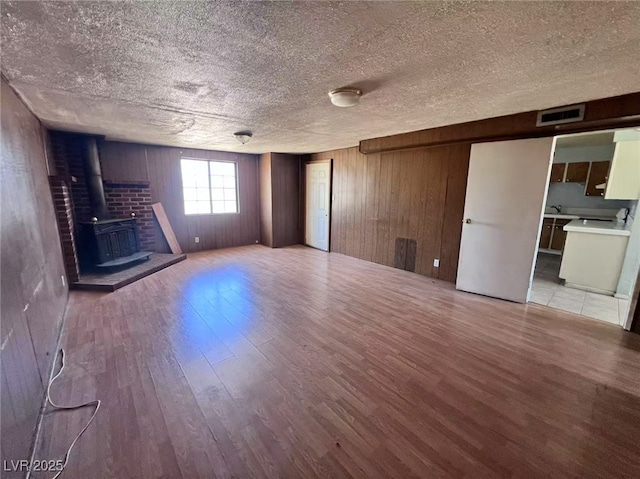 6120 Denver Cir, Las Vegas, NV 89107 - unfurnished living room with wood finished floors, a wood stove, a textured ceiling, and wood walls
