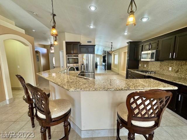 3197 Dusty Moon Ave, Henderson, NV 89052 - kitchen with appliances with stainless steel finishes, arched walkways, tasteful backsplash, a spacious island, and hanging light fixtures