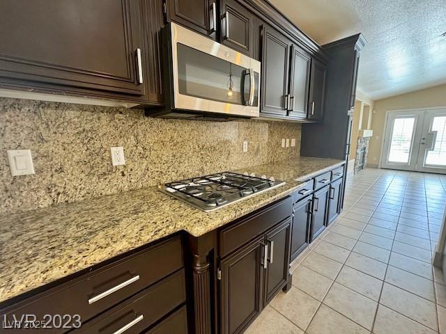 3197 Dusty Moon Ave, Henderson, NV 89052 - kitchen featuring stainless steel appliances, light tile patterned flooring, a textured ceiling, tasteful backsplash, and vaulted ceiling