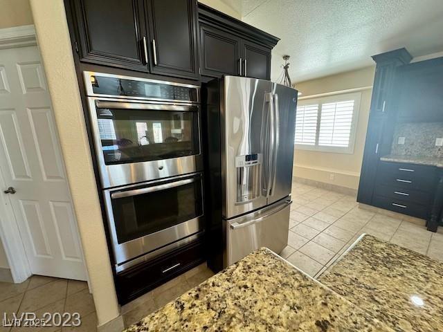3197 Dusty Moon Ave, Henderson, NV 89052 - kitchen featuring appliances with stainless steel finishes, light tile patterned flooring, light stone countertops, a textured ceiling, and dark cabinetry