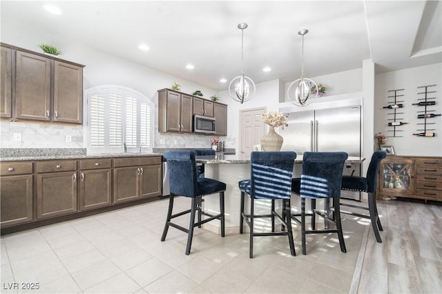 10183 Cascadia Creek St, Las Vegas, NV 89141 - kitchen with appliances with stainless steel finishes, a chandelier, decorative backsplash, a kitchen bar, and light stone countertops