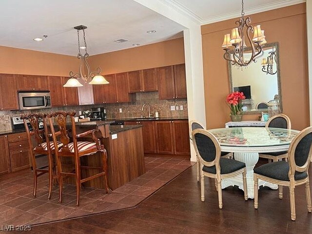 2405 Serene Ave Unit 241, Las Vegas, NV 89123 - kitchen featuring stainless steel microwave, brown cabinetry, dark countertops, a chandelier, and ornamental molding