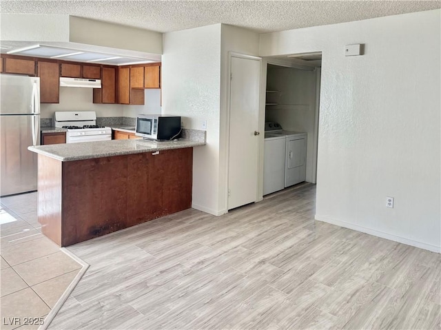 805 Rock Springs Dr Unit 101, Las Vegas, NV 89128 - kitchen featuring washer and clothes dryer, appliances with stainless steel finishes, a textured ceiling, brown cabinetry, and a peninsula