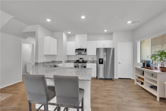 4650 Blaise Ave Unit 102, North Las Vegas, NV 89084 - kitchen with stainless steel appliances, a peninsula, light stone counters, white cabinets, and recessed lighting
