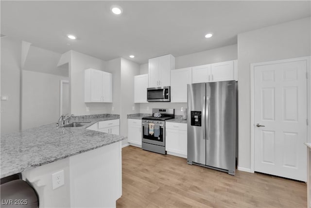 4650 Blaise Ave Unit 102, North Las Vegas, NV 89084 - kitchen featuring stainless steel appliances, light stone counters, a peninsula, light wood finished floors, and white cabinetry