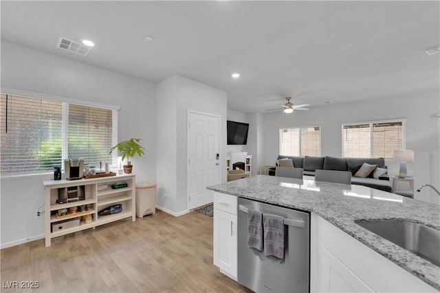 4650 Blaise Ave Unit 102, North Las Vegas, NV 89084 - kitchen with stainless steel dishwasher, ceiling fan, white cabinets, light stone countertops, and a warm lit fireplace