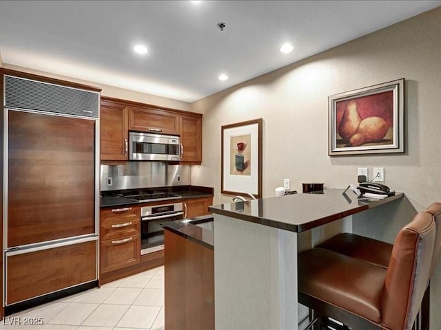 125 E Harmon Ave Unit 220, Las Vegas, NV 89109 - kitchen featuring stainless steel appliances, dark countertops, brown cabinets, a peninsula, and a kitchen breakfast bar