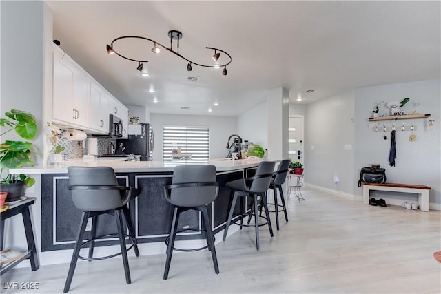 441 Groft Way, Henderson, NV 89015 - kitchen with light countertops, a peninsula, white cabinetry, light wood finished floors, and decorative backsplash