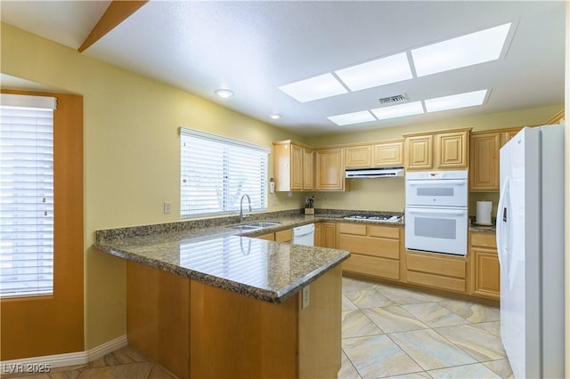 3016 Lotus Hill Dr, Las Vegas, NV 89134 - kitchen with a peninsula, white appliances, dark countertops, a skylight, and light brown cabinets