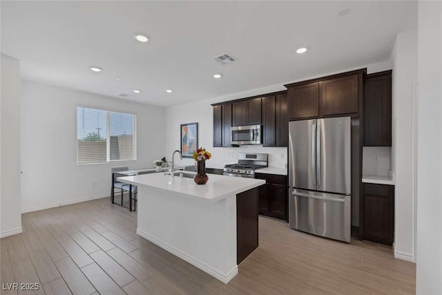 9827 Mojave Mountain St, Las Vegas, NV 89166 - kitchen with appliances with stainless steel finishes, a center island with sink, light wood-style flooring, dark brown cabinets, and light countertops