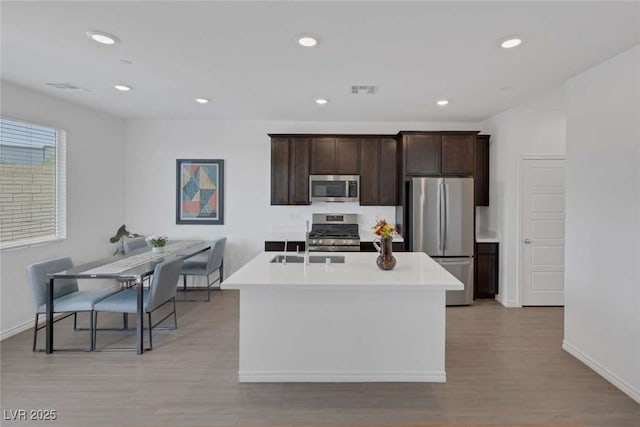 9827 Mojave Mountain St, Las Vegas, NV 89166 - kitchen featuring appliances with stainless steel finishes, light countertops, dark brown cabinets, a kitchen island with sink, and light wood-style floors