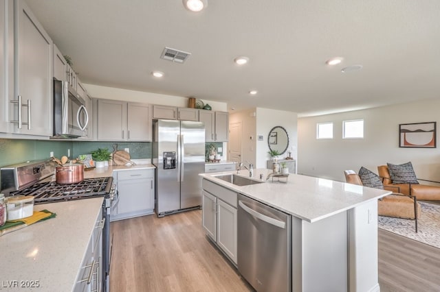 1321 Gable Falls Dr Unit 58, North Las Vegas, NV 89084 - kitchen with stainless steel appliances, gray cabinets, light wood-style flooring, a center island with sink, and light stone counters