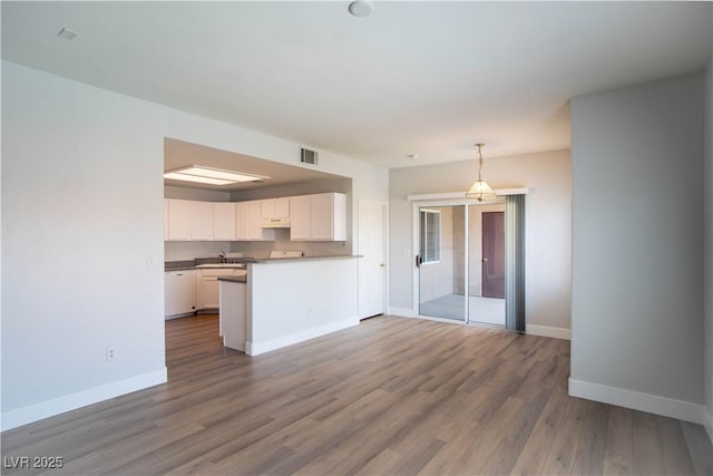 9580 W Reno Ave Unit 240, Las Vegas, NV 89148 - kitchen featuring white cabinets, a peninsula, wood finished floors, decorative light fixtures, and open floor plan