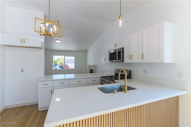 6760 Fallona Ave, Las Vegas, NV 89156 - kitchen featuring a peninsula, stainless steel appliances, vaulted ceiling, light wood-type flooring, and white cabinets