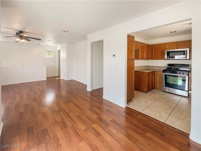 8872 Niche Ave, Las Vegas, NV 89149 - kitchen featuring open floor plan, brown cabinetry, stainless steel appliances, light wood-style floors, and light countertops