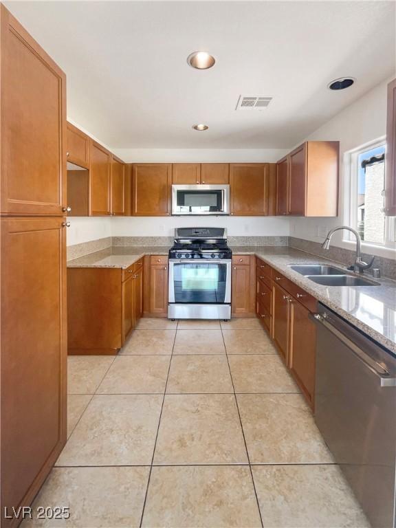 8872 Niche Ave, Las Vegas, NV 89149 - kitchen featuring appliances with stainless steel finishes, brown cabinetry, light stone countertops, light tile patterned flooring, and recessed lighting