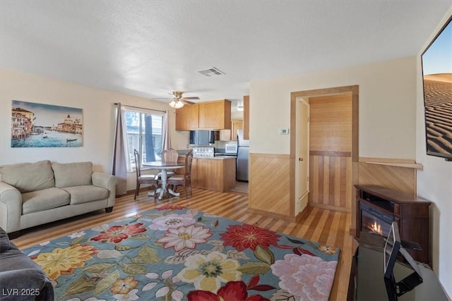 1481 Lorilyn Ave Unit 1, Las Vegas, NV 89119 - living room with a wainscoted wall, light wood-style floors, a glass covered fireplace, wood walls, and a ceiling fan