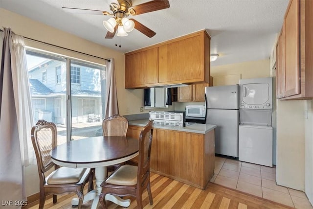 1481 Lorilyn Ave Unit 1, Las Vegas, NV 89119 - kitchen with stacked washer and clothes dryer, freestanding refrigerator, a peninsula, a ceiling fan, and brown cabinetry