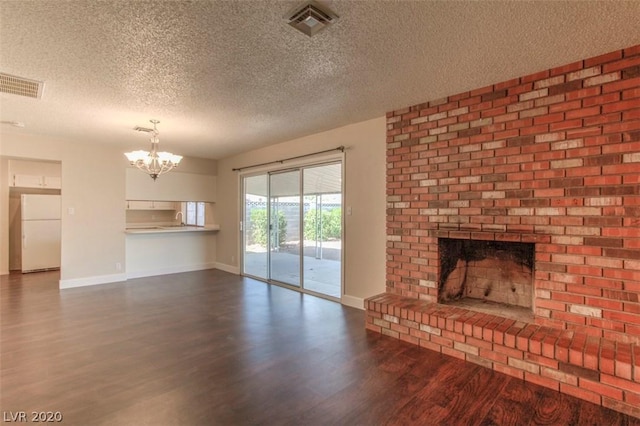 unfurnished living room featuring a chandelier, a brick fireplace, dark wood-type flooring, and a textured ceiling