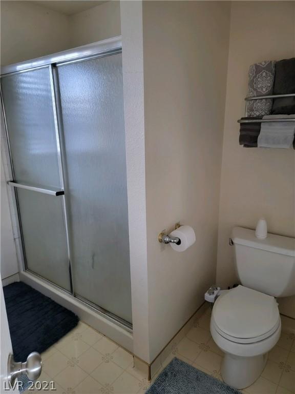 bathroom with tile floors, toilet, and a shower with door