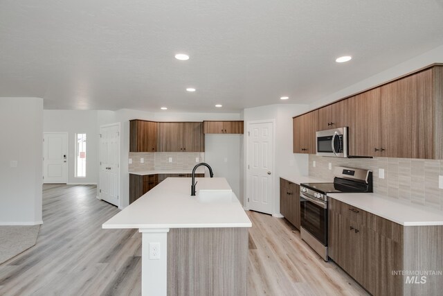 kitchen with decorative backsplash, appliances with stainless steel finishes, light hardwood / wood-style floors, and an island with sink