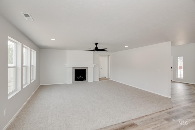 unfurnished living room with a fireplace, a wealth of natural light, light hardwood / wood-style flooring, and ceiling fan