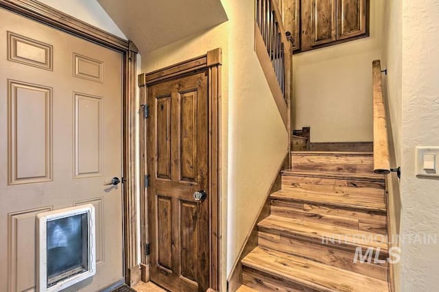 stairway featuring vaulted ceiling and a textured wall