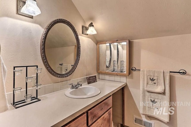 bathroom featuring vaulted ceiling, visible vents, vanity, and a textured wall