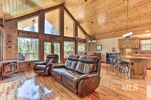 living area featuring a wood stove, high vaulted ceiling, light wood-type flooring, a chandelier, and wood ceiling