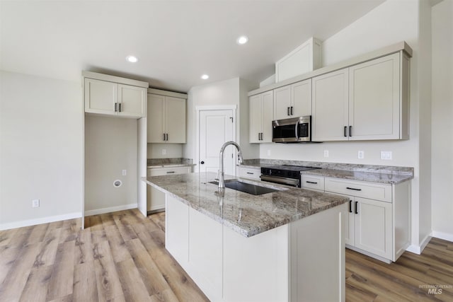 kitchen with appliances with stainless steel finishes, light stone countertops, a sink, baseboards, and light wood-style floors