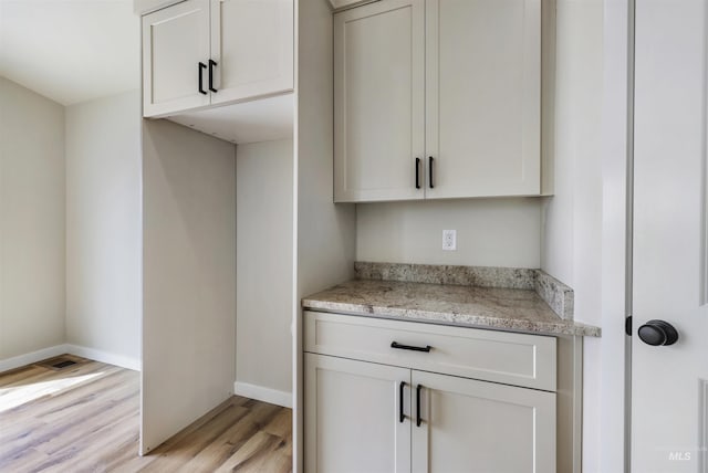 kitchen featuring light wood-style floors, baseboards, light stone countertops, and white cabinetry
