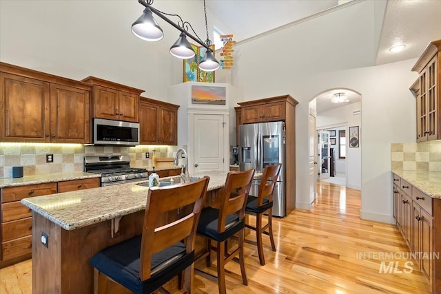 kitchen featuring backsplash, a kitchen island with sink, stainless steel appliances, and high vaulted ceiling