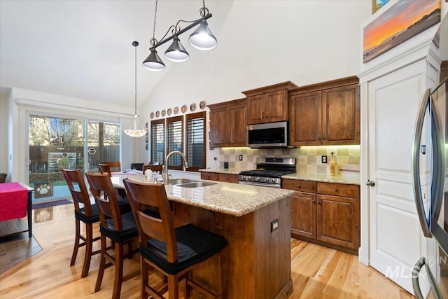 kitchen featuring high vaulted ceiling, backsplash, decorative light fixtures, a kitchen island with sink, and appliances with stainless steel finishes