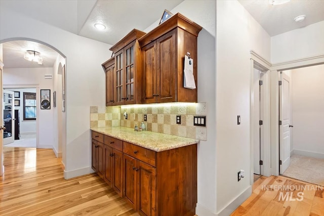 kitchen with a textured ceiling, light stone counters, light hardwood / wood-style flooring, and tasteful backsplash