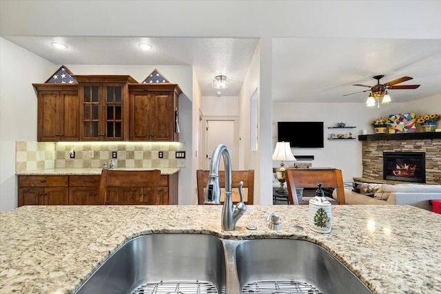 kitchen with a stone fireplace, decorative backsplash, sink, and light stone counters