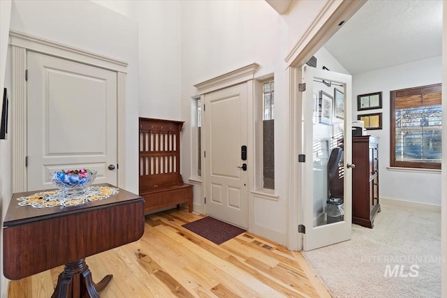 foyer entrance featuring plenty of natural light, lofted ceiling, and light hardwood / wood-style flooring