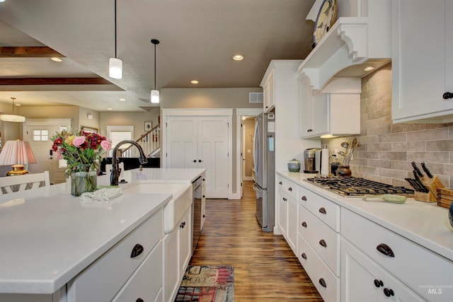 kitchen with appliances with stainless steel finishes, dark hardwood / wood-style flooring, an island with sink, and decorative light fixtures