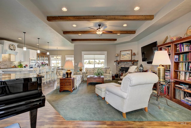 living room with a stone fireplace, beamed ceiling, ceiling fan with notable chandelier, and dark hardwood / wood-style flooring