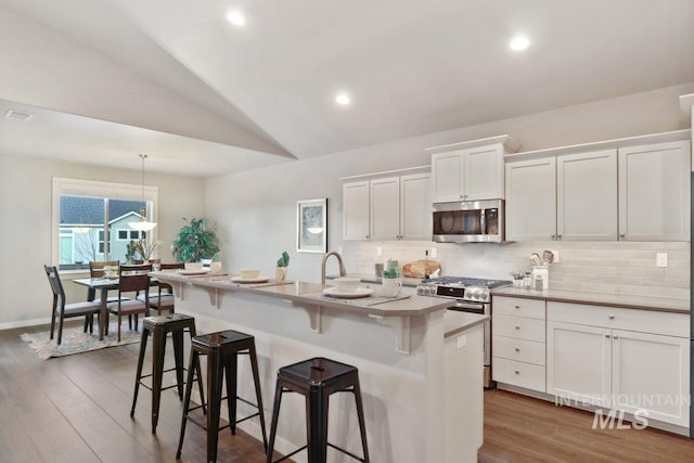 kitchen with white cabinetry, appliances with stainless steel finishes, vaulted ceiling, and a center island with sink