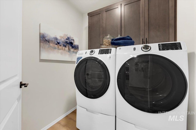 washroom with cabinets, washing machine and clothes dryer, and light hardwood / wood-style floors